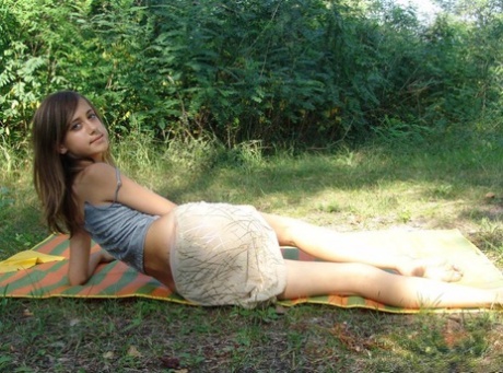 Young looking girl exposes her bellybutton on a blanket near some trees 22106240