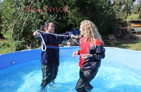 Blonde girl is restrained in rainwear by a lesbian in a backyard pool